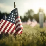 Honoring Our Fallen Heroes - Memorial Day. The U.S. flag waves in the background with a serene and respectful tone. A soldier's helmet rests on a rifle, accompanied by military boots and poppies, symbolizing remembrance. The text is in an elegant, respectful font, evoking gratitude and reverence for those who sacrificed their lives in military service.